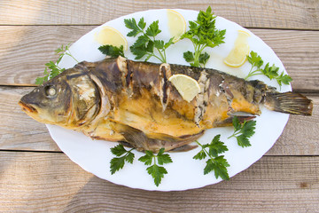 Tasty baked carp in white plate on wooden table. Top view