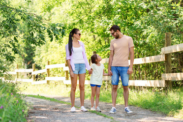 Obraz premium family, leisure and people concept - happy mother, father and little daughter walking in summer park