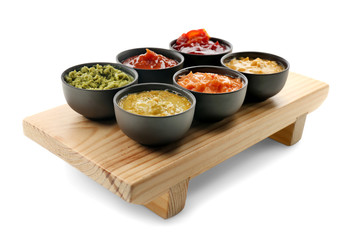 Wooden stand with tasty sauces in bowls on white background