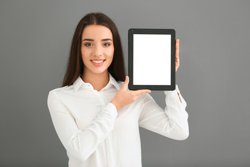 Young woman holding tablet computer on grey background