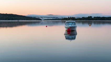 A motor boat moored on the calm waters of Loch Lomond - 232275173