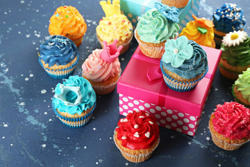 Tasty cupcakes and birthday gift on color background