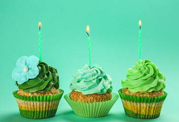 Tasty birthday cupcakes with burning candles on color background