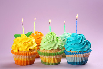 Tasty birthday cupcakes with burning candles on color background