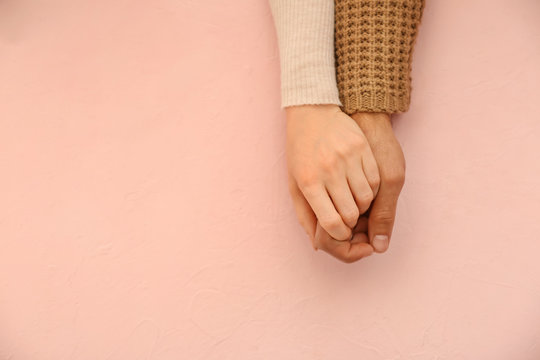 Loving young couple holding hands on color background