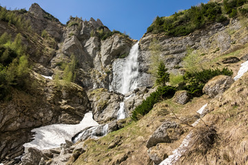 Fototapeta na wymiar spring mountain waterfall, with green vegetation and snow on a blue sky 