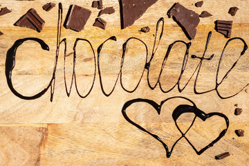 Inscription chocolate written with melted chocolate on wooden background, copy space