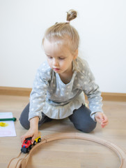 Naklejka premium Little Caucasian Girl Playing with Wooden Railway at Home Early Education Games Funny Development