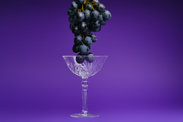 bunch of fresh ripe grapes and glass on purple background