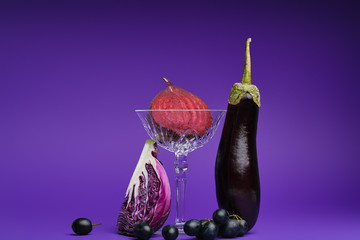 close-up view of halved beetroot in glass, sliced cabbage, grapes and eggplant on purple