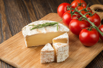 Brie cheese and tomato slice on wood cutting board.