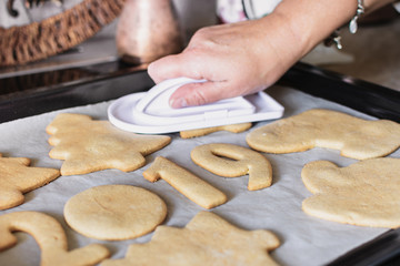 Hot baked Christmas gingerbread cookies are lying on a baking sheet. Female hand smoothes freshly baked gingerbreads with a special pastry spatula
