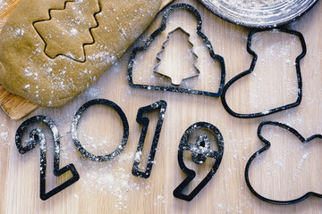 Making Christmas gingerbread at home,  dough and cutters, such as trees, boot, mitten, hat and figures 2019 are on a desk  and ready for making gingerbread
