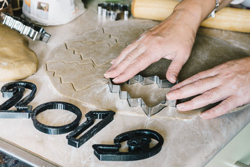 Women's hands cut out a dough as a Christmas tree for gingerbread, next to them are forms for cutting out figures 2019