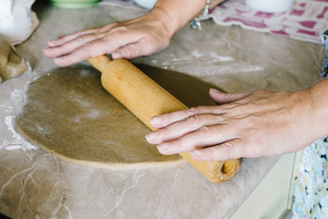 Women's hands rolling dough with a rolling pin into a thin layer for baking Christmas gingerbread