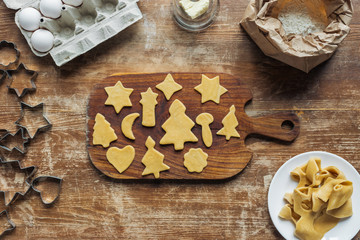 flat lay with cut raw dough for christmas cookies baking on cutting board on wooden surface