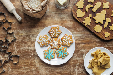 flat lay with Christmas cookies on plate, ingredients and cookie cutters arranged on wooden tabletop