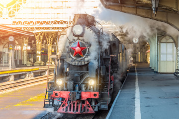 Retro steam train stands on the vintage railway station.