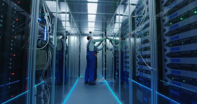 Wide movement stabilized shot of two people working in a data center carrying cable to repair rows of server racks and discuss their work