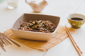 buckwheat noodles with green vegetables in a square plate with Chinese chopsticks on the table