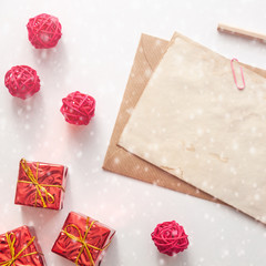 A real photo of bright Christmas card with red presents, rattan balls, a wooden pencil and an old stained paper mockup with snowflakes