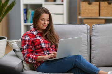 Portrait of an attractive young woman using laptop computer while relaxing on a sofa at home
