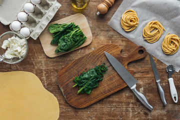 Fototapeta na wymiar top view of cut spinach on wooden chopping board and pasta ingredients