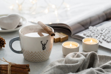 Fototapeta na wymiar Cozy winter still life: mug of hot cacao, opened magazine, two tea candles and Christmas tree lights