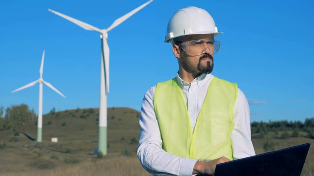 An engineer is operating a laptop in front of windmills. Clean, eco-friendly energy concept.