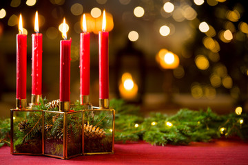 Background of glass and gold candleholder with red candles and spruce branches on red table cloth....