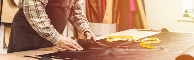 partial view of male handbag craftsman cutting leather by scissors at workshop