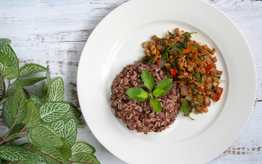 Mixed brown rice and fried pork chopped with basil leaves on white wooden table,Thailand