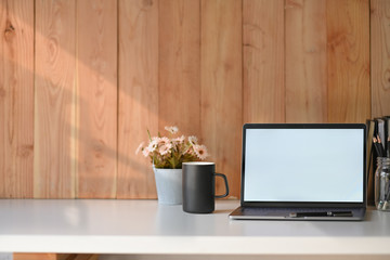 Workplace white table with blank screen laptop, flower, books and coffee mug