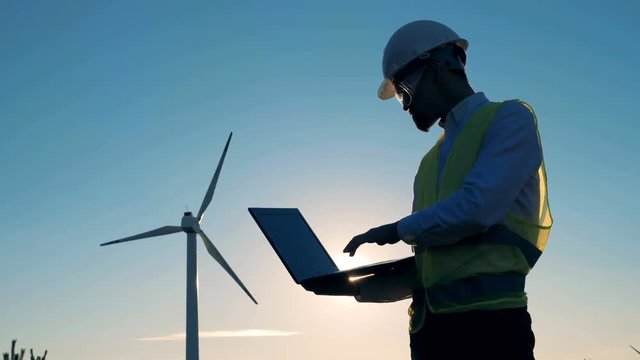 Revolving aeromotor with a male engineer being near it. Renewable alternative energy, environment friendly concept.