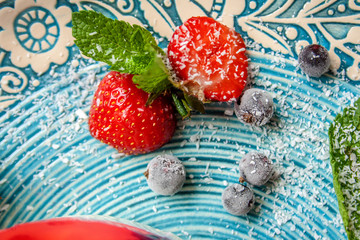 Strawberry closeup view with mint and frozen blueberries on a plate