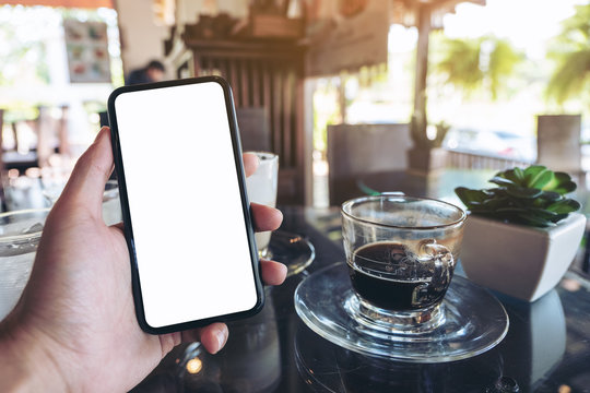 Mockup image of a hand holding black mobile phone with blank desktop screen in cafe
