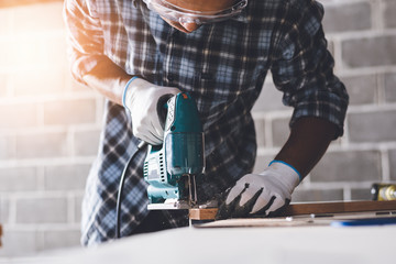 Confident wood worker expert. Young man working at factory. Skilled carpenter cutting a piece of...
