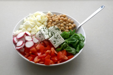 Bowl of healthy salad with feta cheese, tomato, radish, cucumber, chickpeas, lamb's lettuce and herbs. Selective focus. 