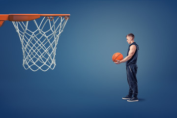 A young athlete with a basketball ball in his hands stands near an orange hoop.