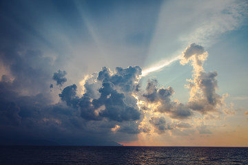 Sun rays and dark clouds on sky at the sea before sunset in the evening