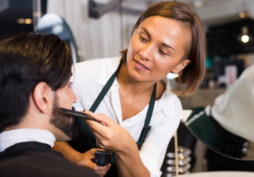 woman hairdresser shaving man's beard in barbershop