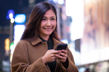 Young Asian woman in city at night texting on cell phone