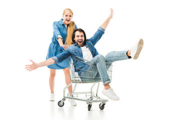 excited couple laughing and having fun with shopping cart isolated on white