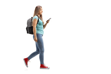 Female student with backpack walking and using a mobile phone