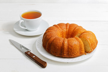 Homemade round lemon cake soaked with lemon syrup and cup of tea on white wooden table