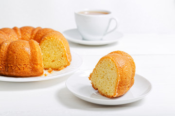 Homemade round lemon cake soaked with lemon syrup and cup of tea on white wooden table
