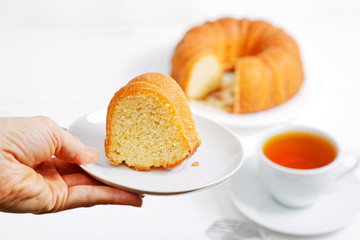 Closeup hand is holding a saucer with a piece of lemon cake.  Homemade pie and cup of tea on a blurred background. Shallow focus.