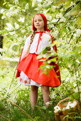 Smiling blond girl posing in a dress of little red riding hood near green trees