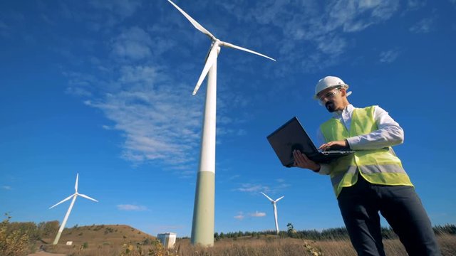 A set of windmills with a male engineer operating his laptop next to it. Clean, eco-friendly energy concept.