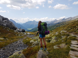 Hiker with backpack walking a grass trail on top of a mountain and enjoying valley view during trip in the alps